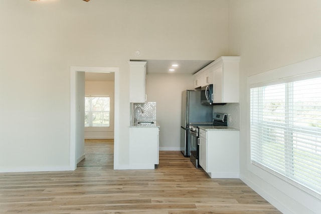 4406 Helen St, Hitchcock, TX 77563 - kitchen featuring white cabinetry, tasteful backsplash, light wood-type flooring, baseboards, and appliances with stainless steel finishes
