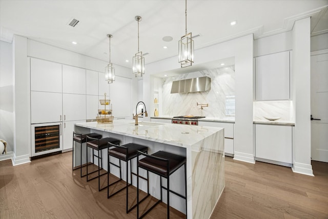 kitchen featuring wall chimney range hood, modern cabinets, a sink, and beverage cooler