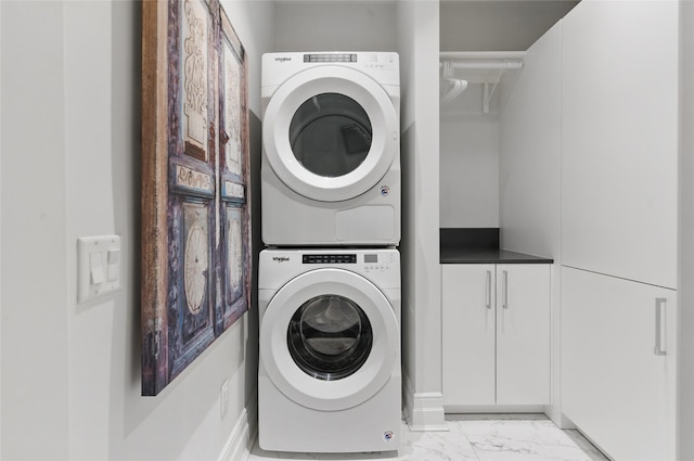 laundry room featuring cabinet space, stacked washer and clothes dryer, and marble finish floor