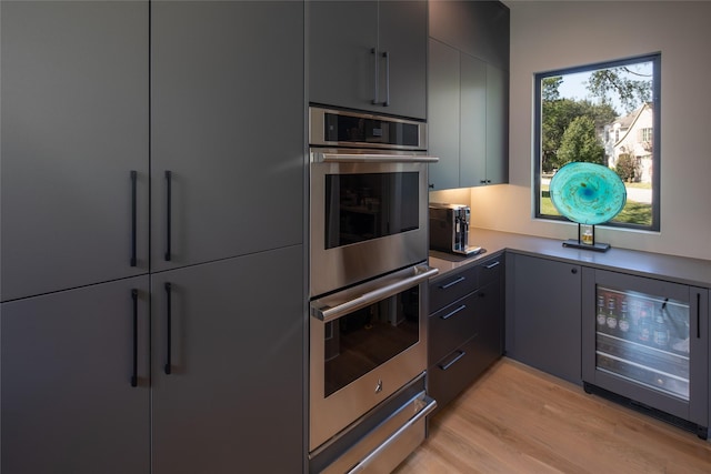 kitchen with beverage cooler, stainless steel double oven, modern cabinets, and light wood-type flooring