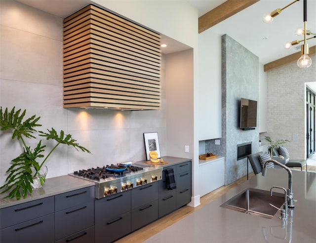 kitchen with a glass covered fireplace, gray cabinets, wall chimney exhaust hood, a sink, and backsplash