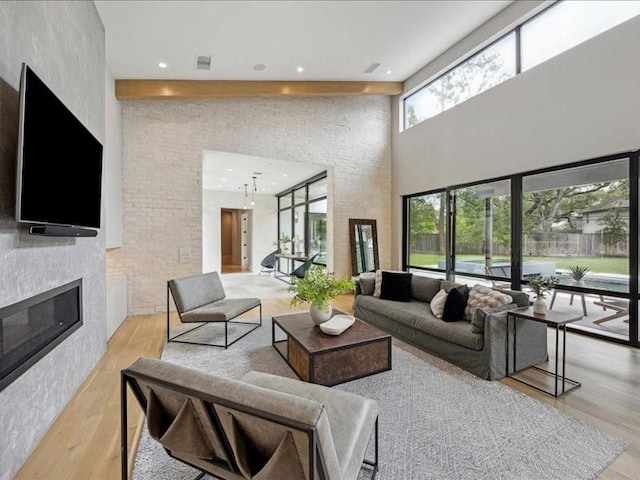 living area featuring a glass covered fireplace, light wood-style floors, recessed lighting, and a towering ceiling
