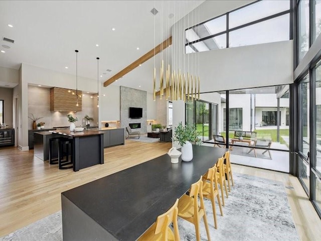 dining room with light wood-type flooring, a towering ceiling, a wealth of natural light, and visible vents