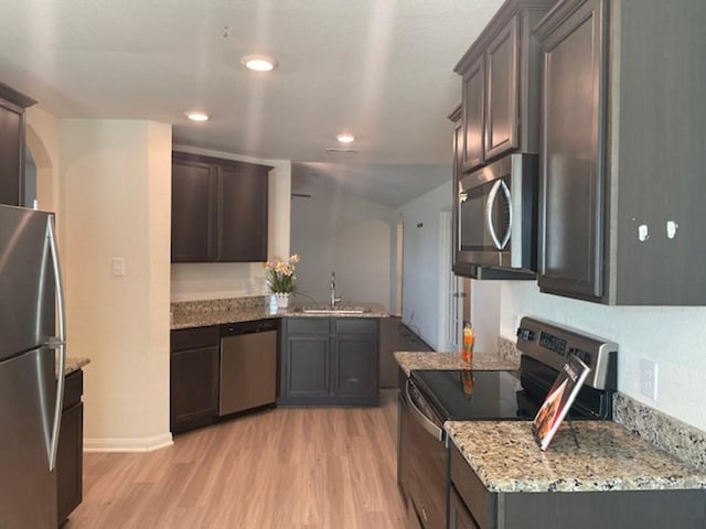 kitchen featuring dark brown cabinetry, a sink, light stone countertops, appliances with stainless steel finishes, and light wood-type flooring
