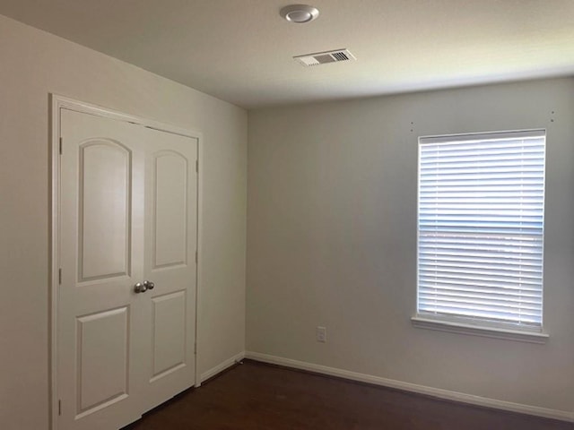 unfurnished bedroom with dark wood finished floors, a closet, baseboards, and visible vents