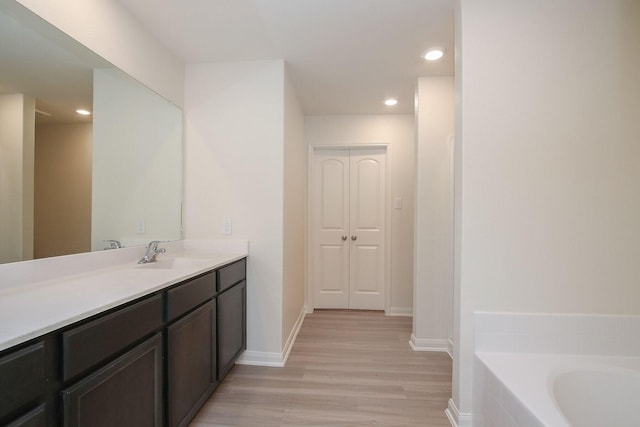 full bath with vanity, recessed lighting, a tub, baseboards, and wood finished floors