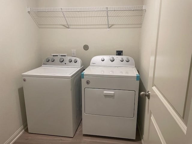 clothes washing area with baseboards, washing machine and dryer, wood finished floors, and laundry area