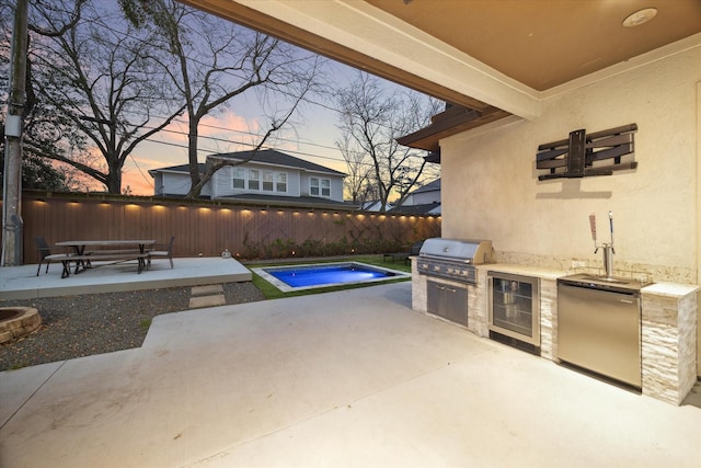 patio terrace at dusk featuring a fenced in pool, an outdoor kitchen, grilling area, wine cooler, and fence
