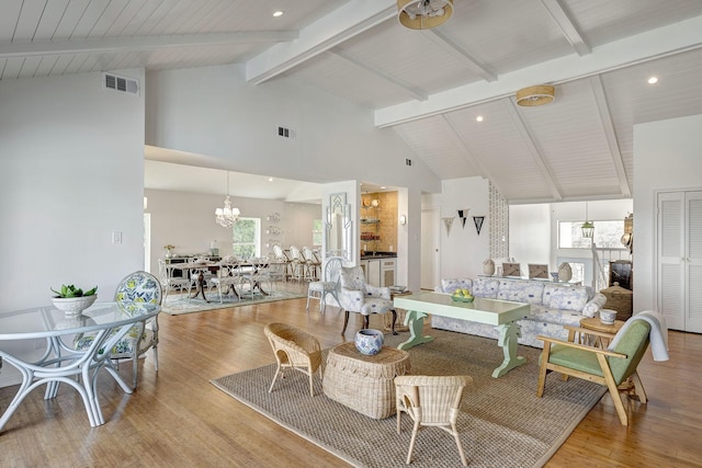 living area featuring high vaulted ceiling, a chandelier, beam ceiling, wood finished floors, and plenty of natural light
