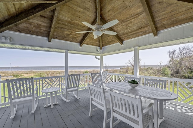deck featuring a ceiling fan, view of water and beach, and outdoor dining space