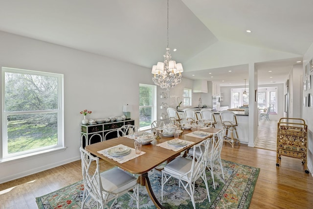 dining area featuring a chandelier, light wood-style flooring, vaulted ceiling, and baseboards