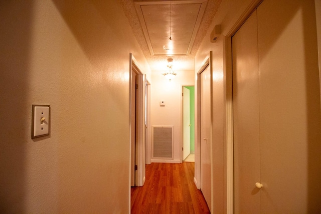 hallway featuring attic access, wood finished floors, and visible vents