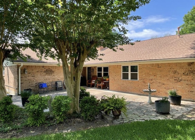 back of property with brick siding, a patio, and a shingled roof