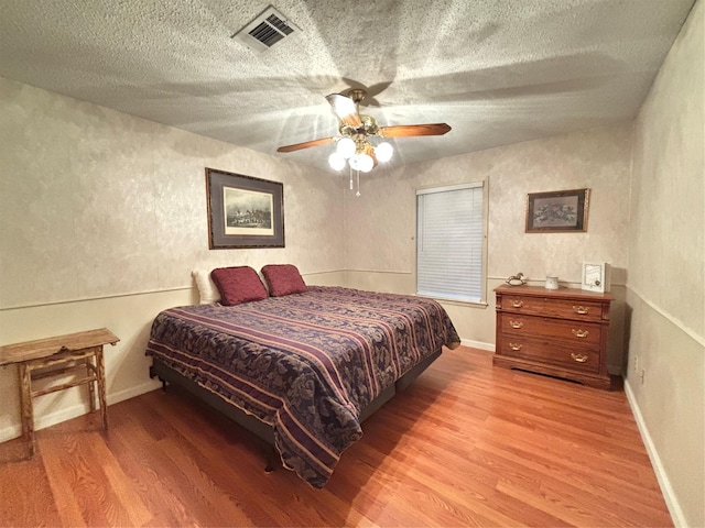 bedroom with a ceiling fan, a textured ceiling, light wood-style floors, a textured wall, and visible vents