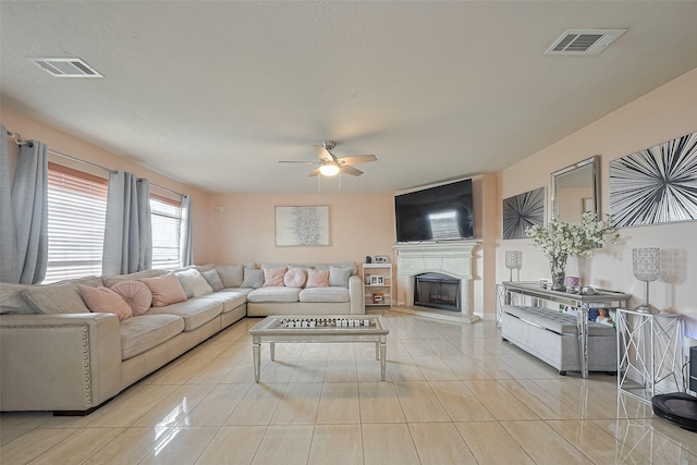 living area with a ceiling fan, tile patterned floors, a fireplace with raised hearth, and visible vents