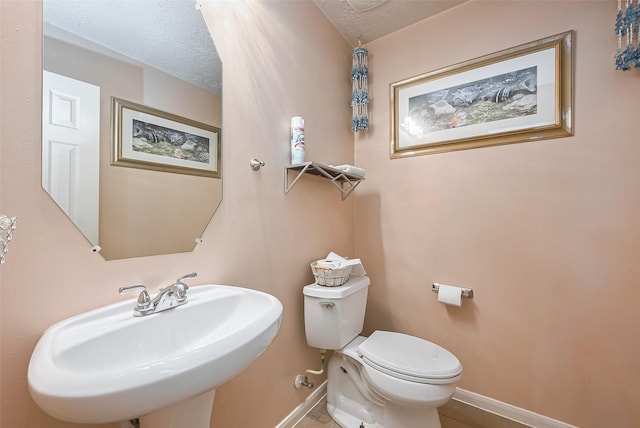 half bath featuring toilet, a sink, baseboards, and a textured ceiling