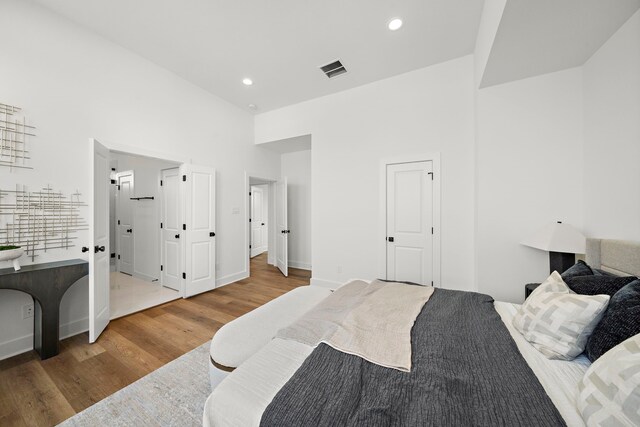 bedroom featuring visible vents, a high ceiling, wood finished floors, and recessed lighting