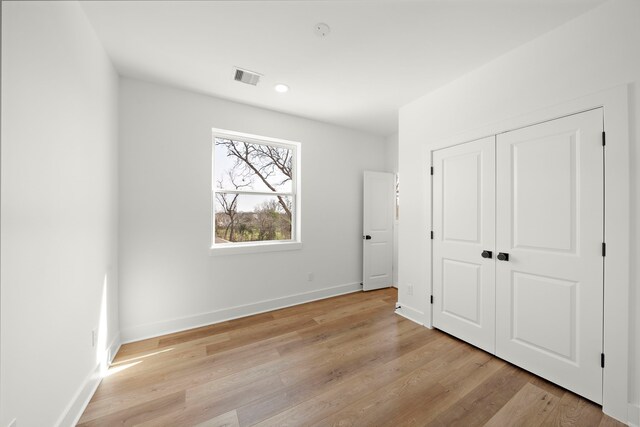 unfurnished bedroom featuring light wood-type flooring, a closet, baseboards, and visible vents