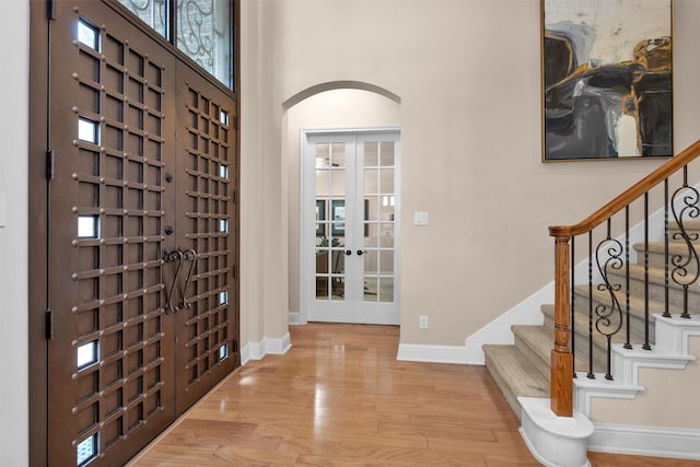 foyer featuring stairs, wood finished floors, baseboards, french doors, and a high ceiling