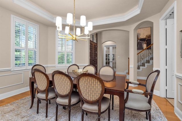 dining area with a tray ceiling, arched walkways, light wood-style floors, crown molding, and a chandelier