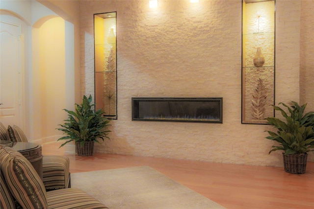 living room with wood finished floors, arched walkways, and a stone fireplace