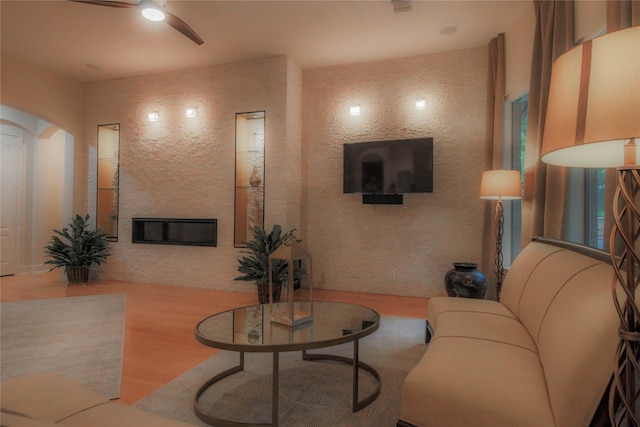 living area with wood finished floors, arched walkways, ceiling fan, and a large fireplace