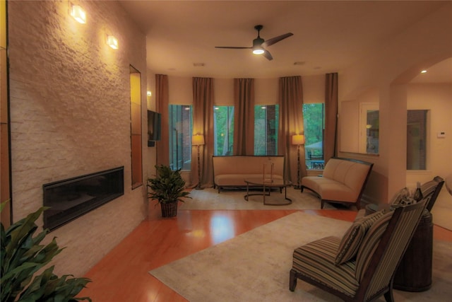 living room with wood finished floors, a fireplace, ceiling fan, and arched walkways