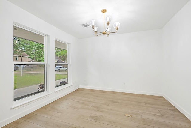 spare room with light wood-style floors, baseboards, visible vents, and a notable chandelier