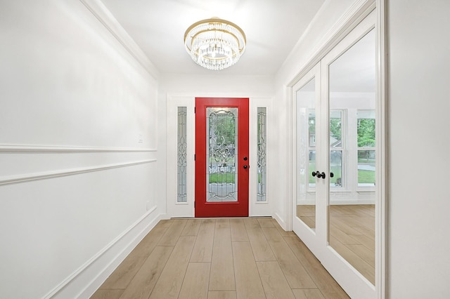 foyer entrance featuring baseboards, light wood finished floors, and a notable chandelier
