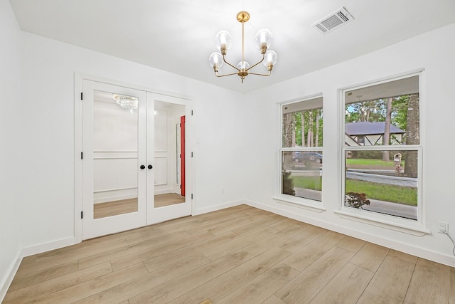empty room featuring visible vents, light wood-style flooring, a notable chandelier, and french doors