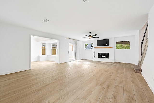 unfurnished living room featuring visible vents, light wood-style floors, baseboards, ceiling fan, and a fireplace with raised hearth