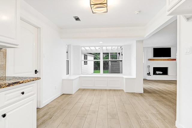 unfurnished dining area with a fireplace with raised hearth and light wood-style flooring