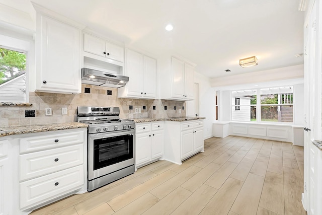 kitchen featuring stainless steel range with gas stovetop, white cabinets, range hood, and tasteful backsplash