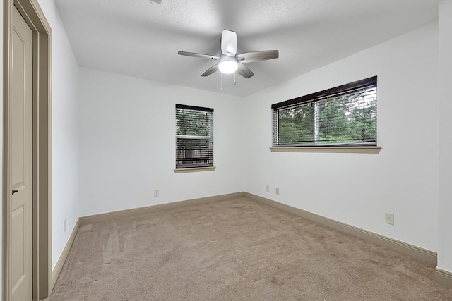carpeted spare room featuring a ceiling fan and baseboards