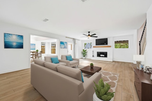 living area with visible vents, a ceiling fan, a glass covered fireplace, and light wood-type flooring