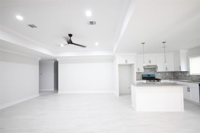 kitchen with gas stove, decorative backsplash, a kitchen island, white cabinets, and a raised ceiling