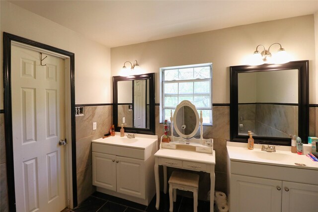 full bathroom featuring tile walls, wainscoting, a sink, and two vanities