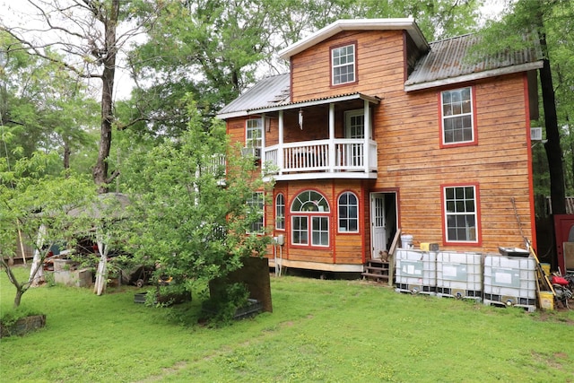 rear view of house with a balcony, metal roof, and a lawn