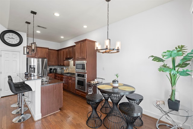 kitchen with wood-type flooring, an inviting chandelier, dark countertops, and stainless steel appliances