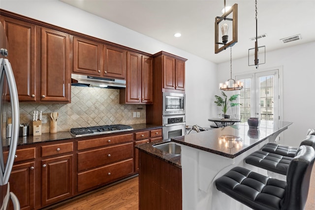 kitchen with visible vents, a breakfast bar, wood finished floors, appliances with stainless steel finishes, and under cabinet range hood