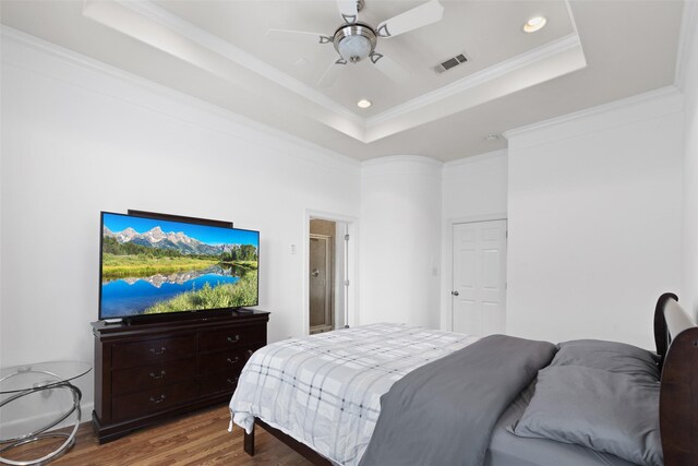 bedroom featuring a tray ceiling, crown molding, a ceiling fan, wood finished floors, and visible vents