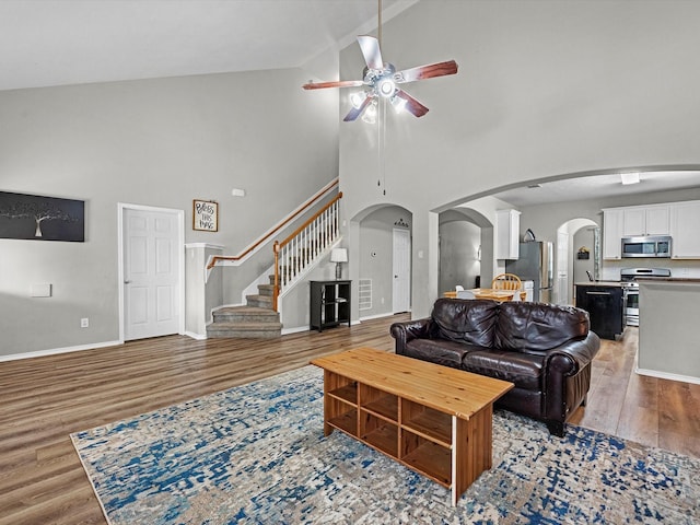 13923 Roanoke Falls Dr, Cypress, TX 77429 - living room featuring a ceiling fan, high vaulted ceiling, light wood-type flooring, stairway, and arched walkways