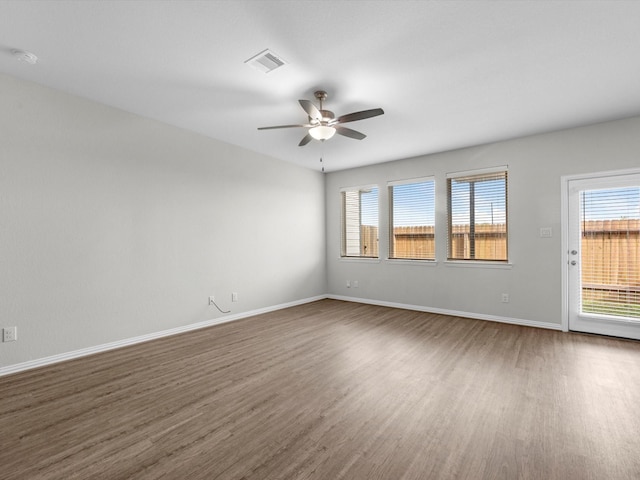empty room featuring plenty of natural light, a ceiling fan, visible vents, and dark wood-type flooring