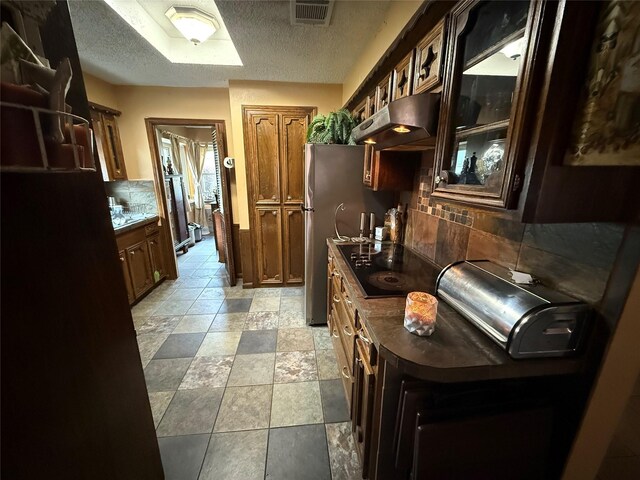 kitchen featuring black electric cooktop, a textured ceiling, visible vents, decorative backsplash, and under cabinet range hood