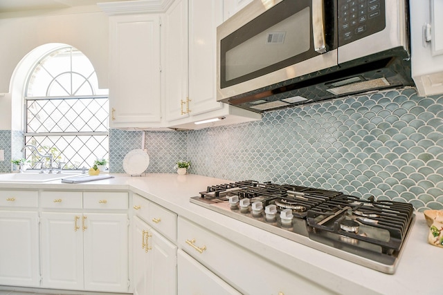 kitchen featuring stainless steel appliances, light countertops, white cabinets, a sink, and tasteful backsplash
