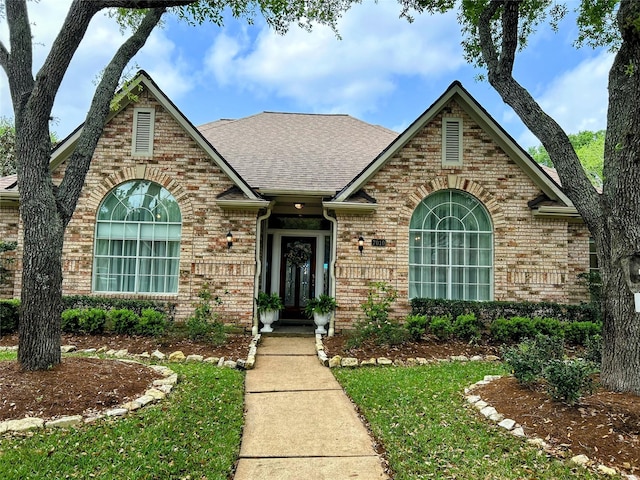 view of front of house with brick siding, roof with shingles, and a front yard