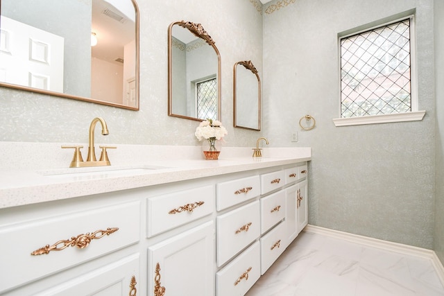full bath featuring marble finish floors, double vanity, and baseboards
