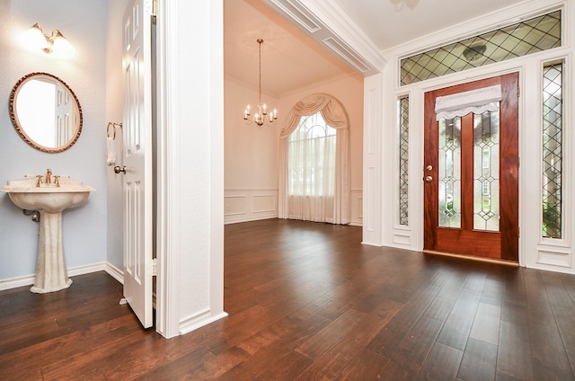 entrance foyer featuring ornamental molding, dark wood-style flooring, a chandelier, a decorative wall, and wainscoting