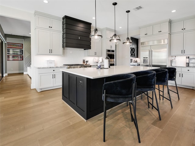 10114 Mariner Oaks Dr, Missouri City, TX 77459 - kitchen with wall chimney range hood, light countertops, light wood finished floors, and visible vents