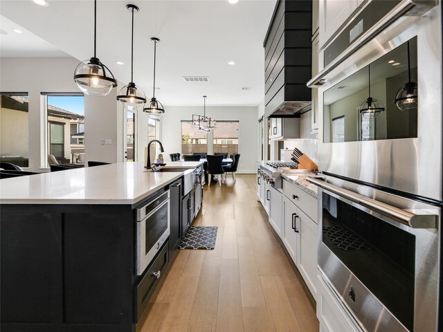 10114 Mariner Oaks Dr, Missouri City, TX 77459 - kitchen featuring an island with sink, light countertops, wood finished floors, appliances with stainless steel finishes, and dark cabinets